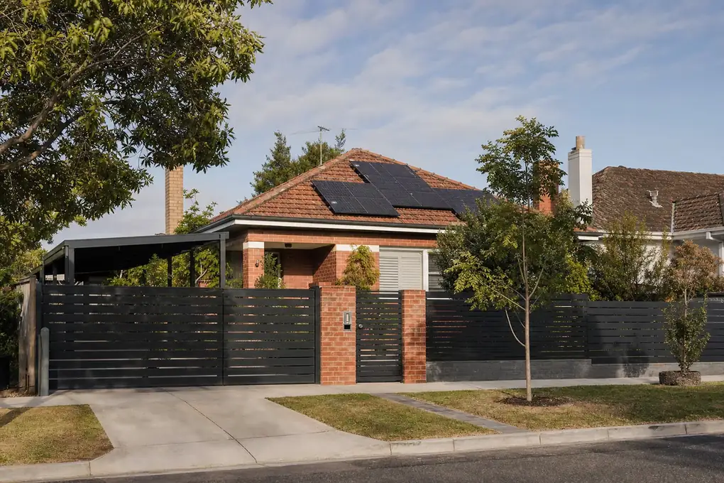Solar battery unit on the rear wall of a Coburg post-war brick home, with rooftop solar panels and a spacious north-facing rear yard visible