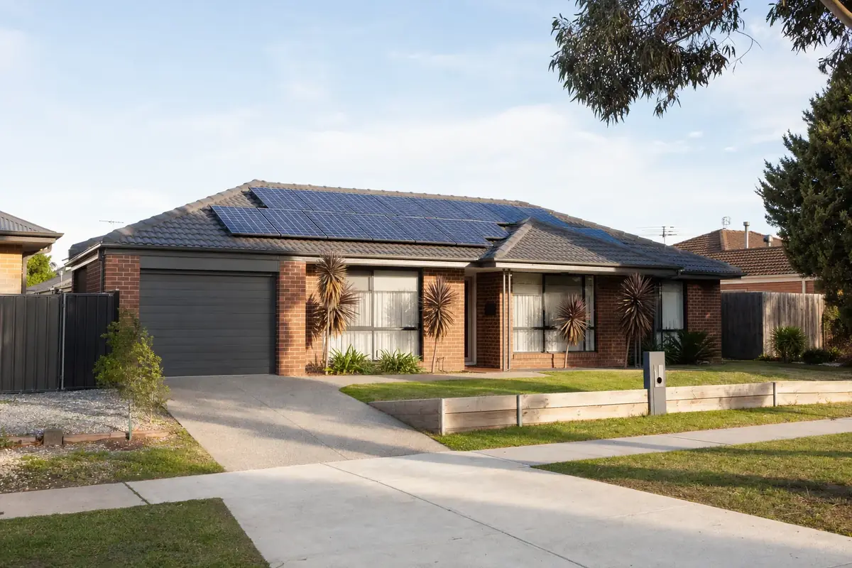 Solar battery on the rear wall of a Dandenong post-war brick home, with north-facing rooftop solar panels and the flat outer south-east Melbourne suburban landscape