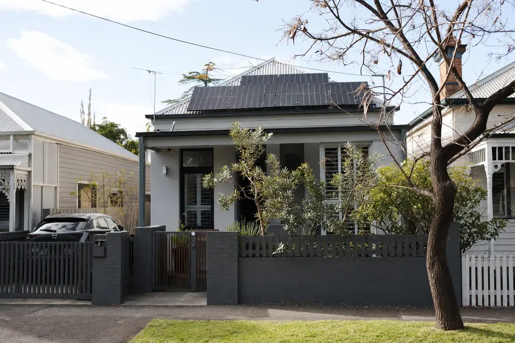 Solar battery on the rear wall of a Footscray post-war workers cottage, with compact rooftop solar panels and the Melbourne CBD skyline visible across the Maribyrnong River