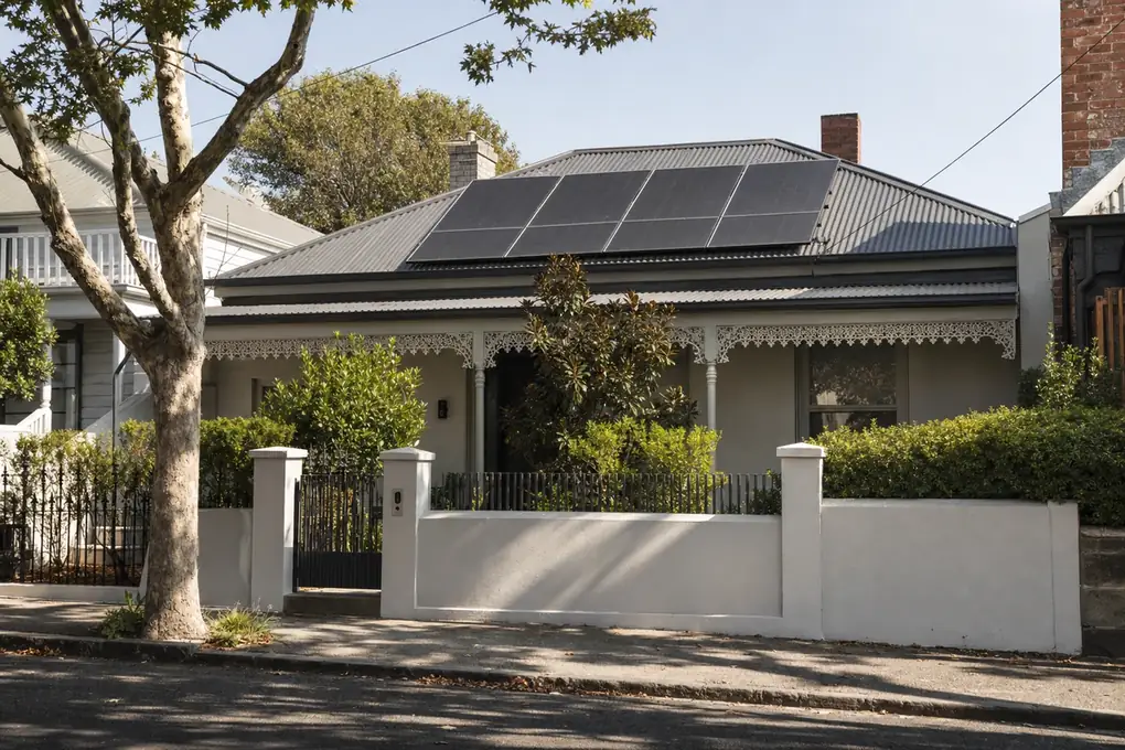 Home battery on the rear brick wall of a Northcote post-war home, with the solar cable conduit running up to rooftop panels on the north-facing slope