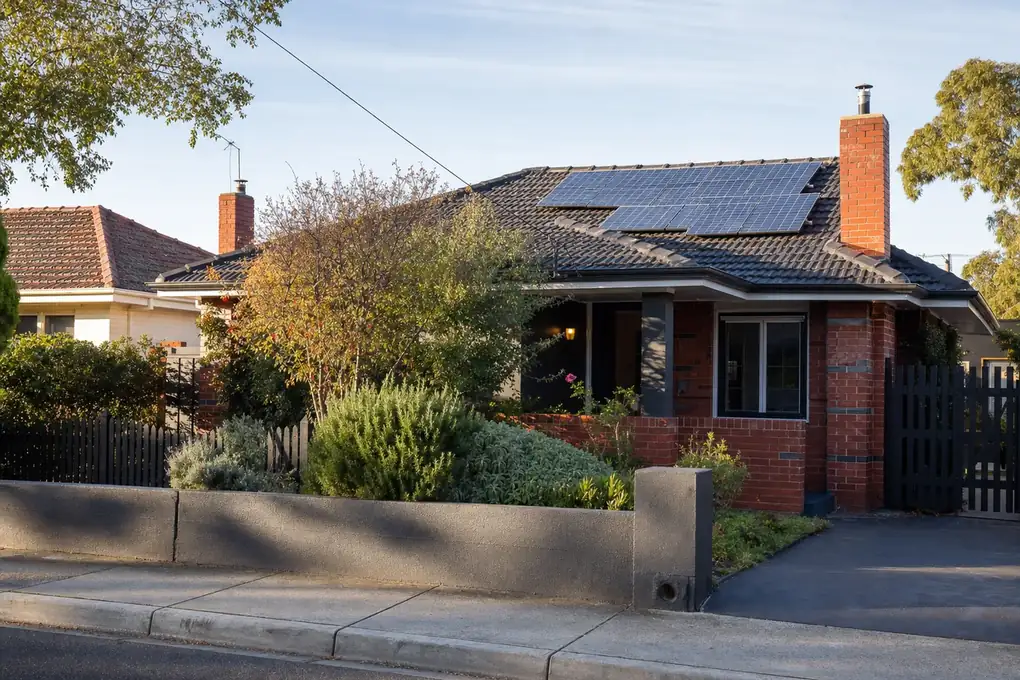 Solar battery and inverter mounted on the side wall of a Preston post-war brick home with high-density solar panels covering the north-facing roof slope