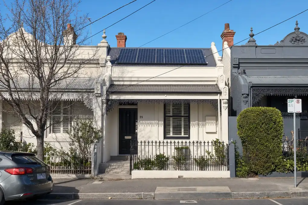 Wall-mounted home battery on a narrow Richmond Victorian terrace home, with the solar inverter mounted beside it and the Melbourne skyline visible in the background